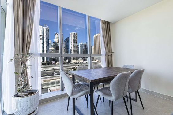 Modern dining area in Global Lake Views, Jumeirah Lakes Towers (JLT), with floor-to-ceiling windows offering a panoramic view of the JLT skyline.